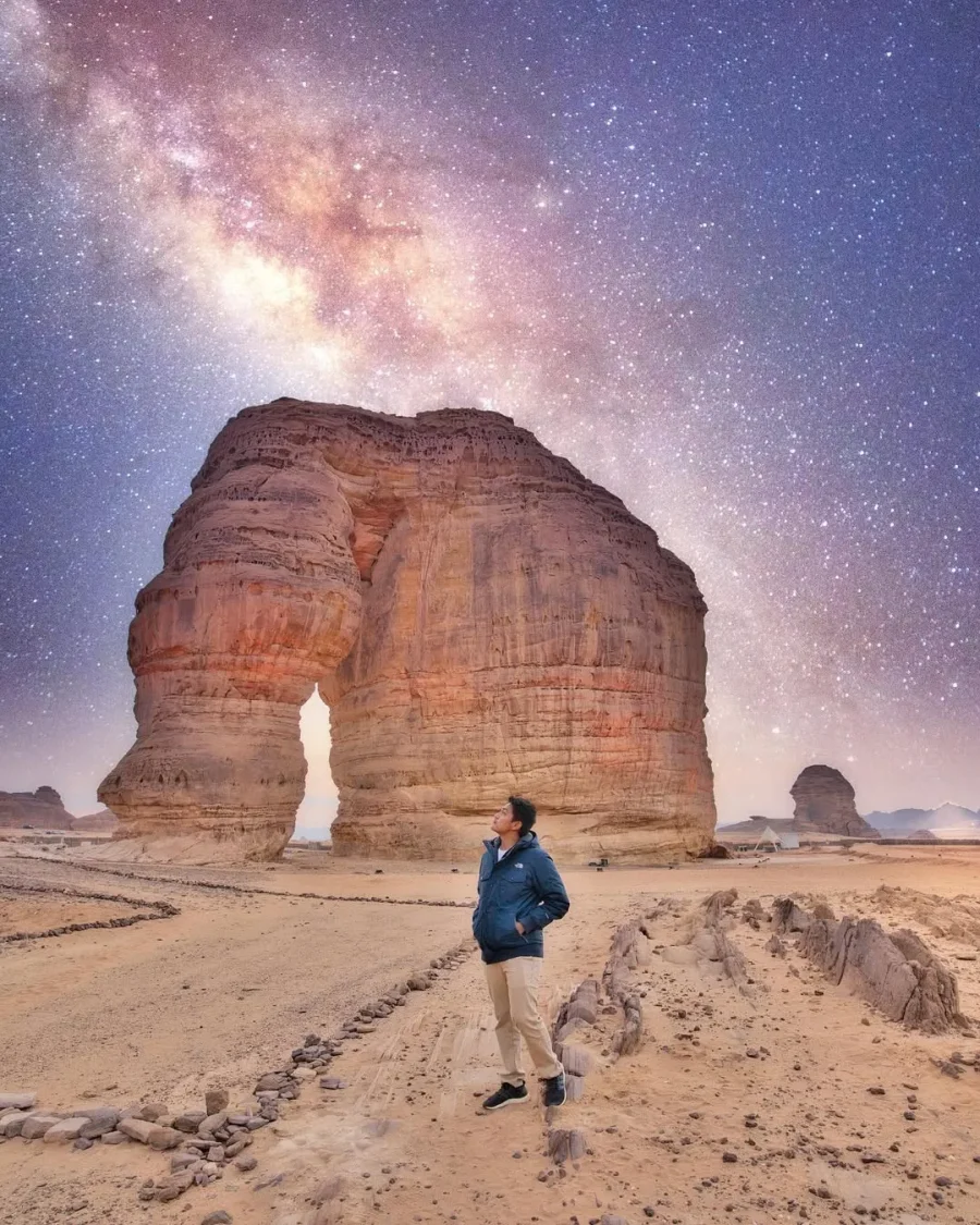 Agung Afif standing beneath a rock arch under a starry sky